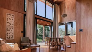 Um quarto espaçoso com piso de madeira, uma mesa de jantar com cadeiras, um sofá e uma grande janela com vista para o exterior.