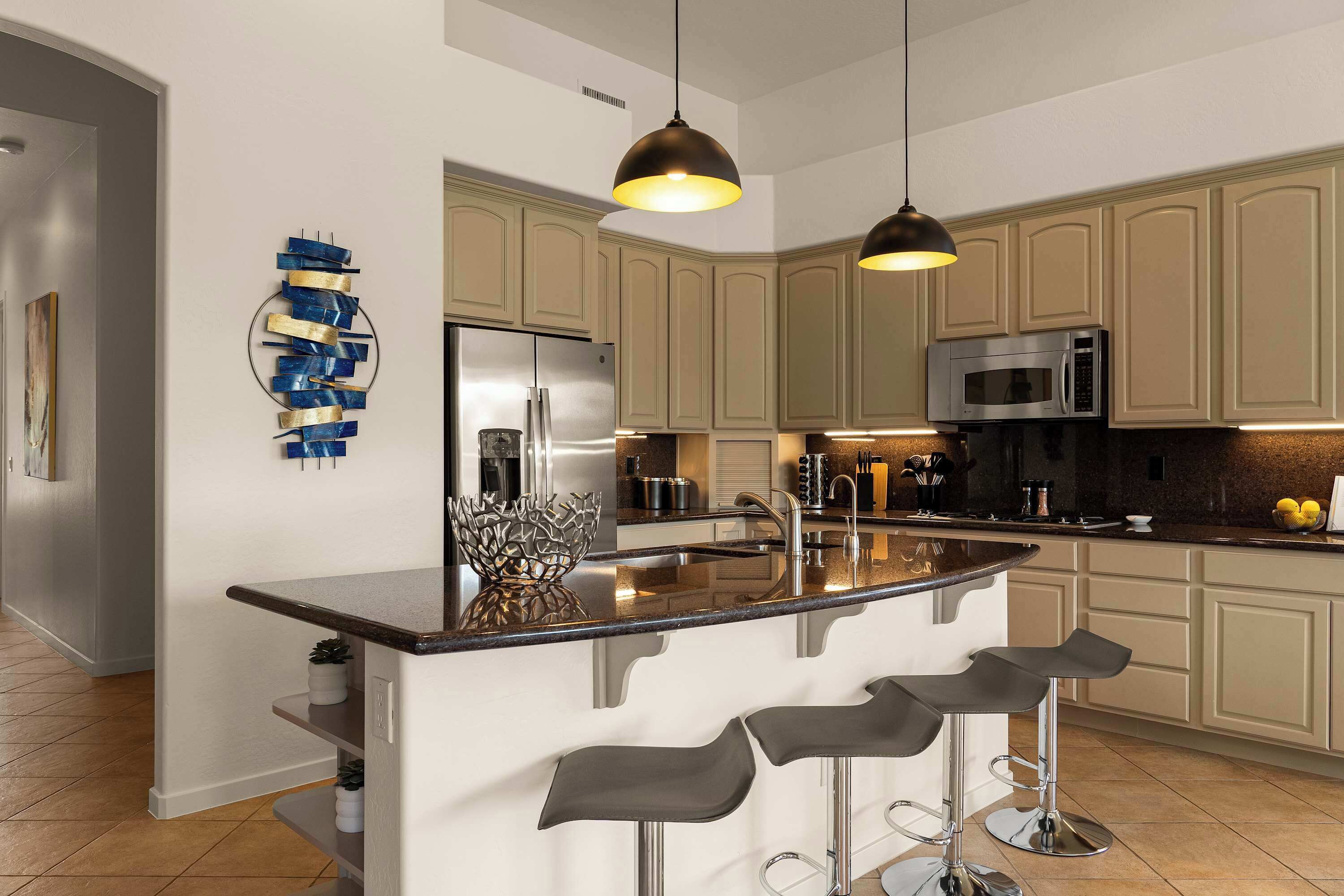 Una cocina moderna con una isla central, taburetes de bar, electrodomésticos de acero inoxidable e iluminación colgante.