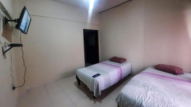 A room with two beds, a television mounted on the wall, and a ceiling light.