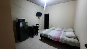 A bedroom with a bed, a desk with a computer, a television, and a door.