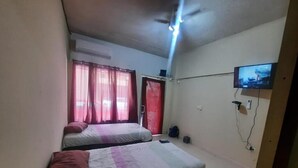 A room with two beds, a ceiling fan, a TV mounted on the wall, and an air conditioning unit.