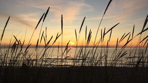 Eine Küstenlandschaft mit hohem Gras im Vordergrund und einem Sonnenuntergang über dem Wasser.
