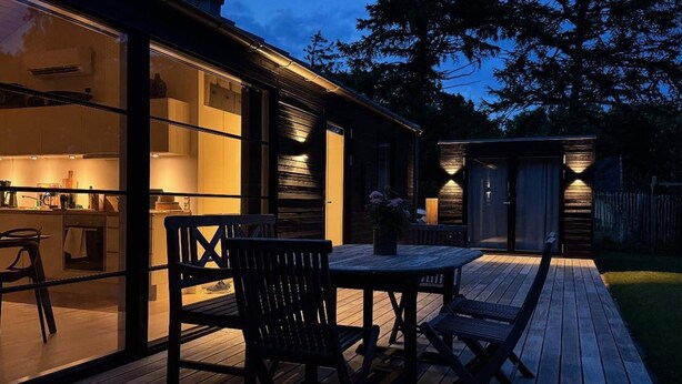 Ein modernes Haus mit Terrasse, Sitzgelegenheiten im Freien und einer gut beleuchteten Küche.