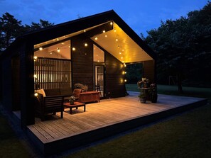 Eine moderne Holzhütte mit einer Terrasse, Sitzgelegenheiten im Freien und Lichterketten.