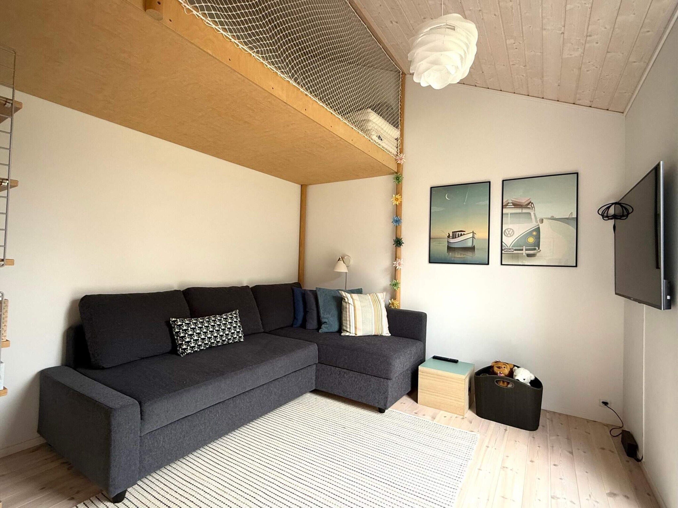 Un soggiorno moderno con un divano ad angolo grigio scuro, una ventola a soffitto bianca e due quadri appesi al muro.
