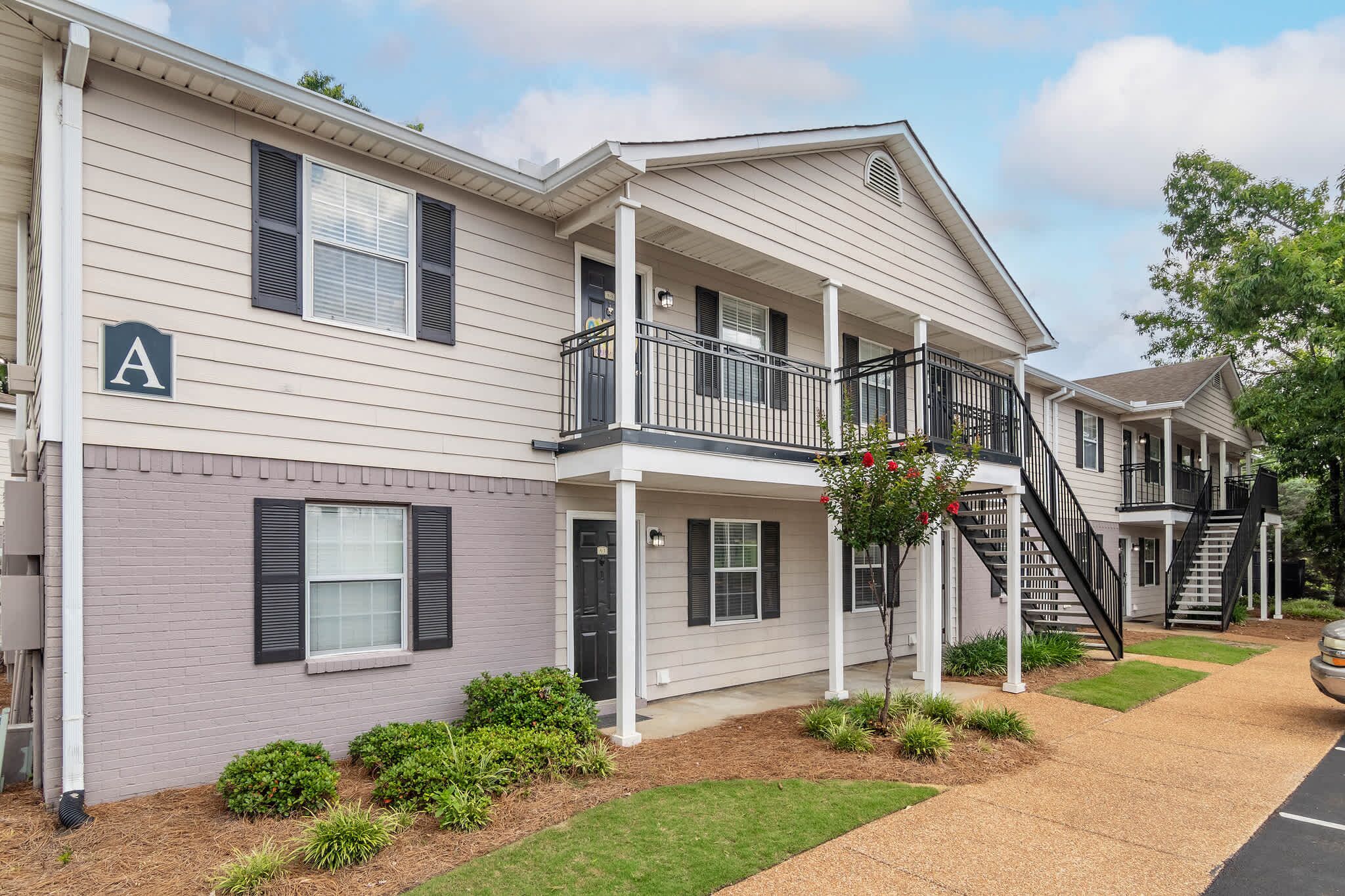A two-story residential building with a covered porch, a staircase, and a small garden area.