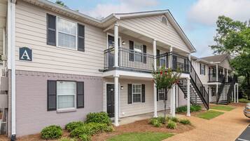 A two-story residential building with a covered porch, a staircase, and a small garden area.