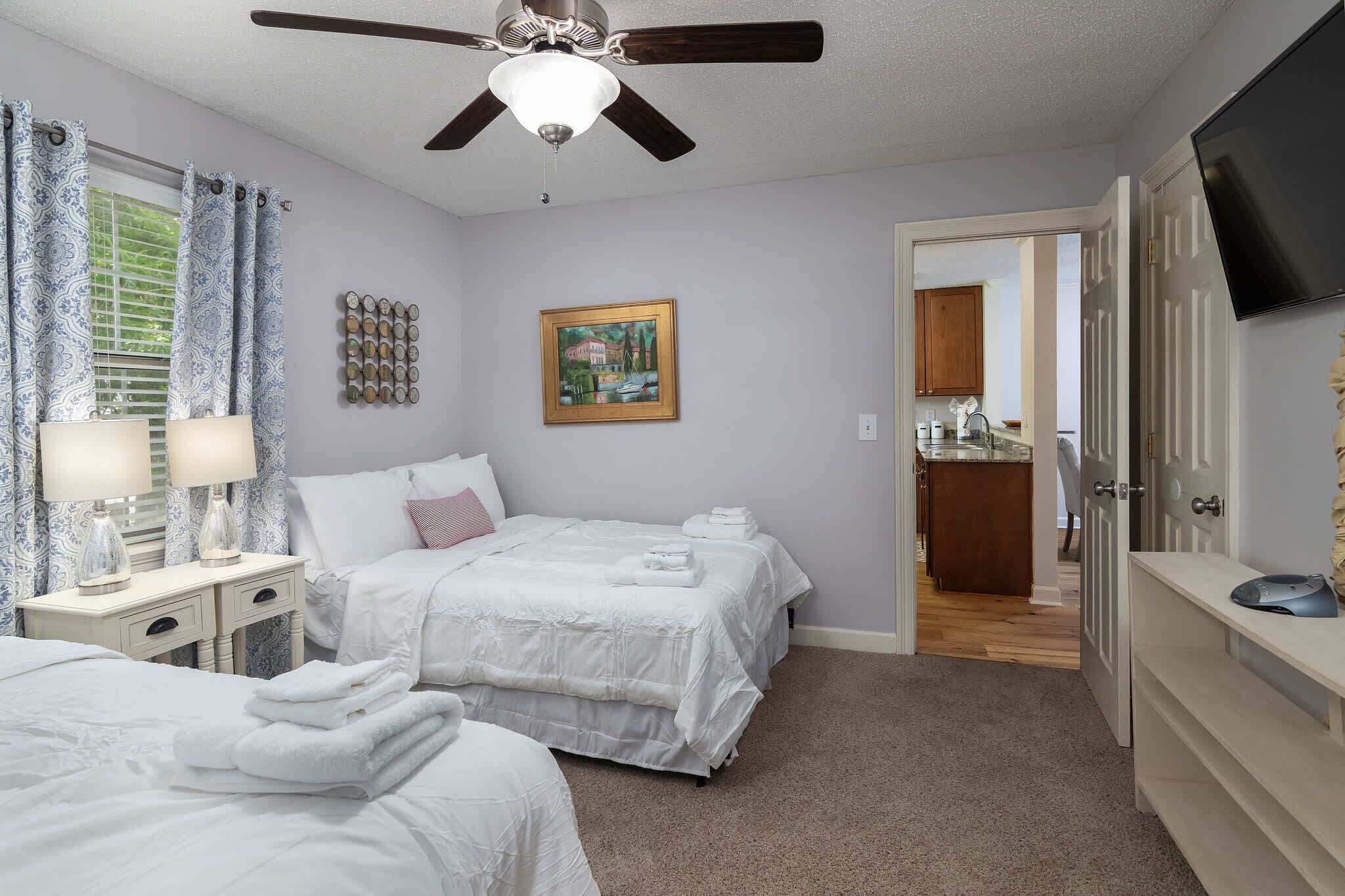 A bedroom with two beds, a ceiling fan, a painting, and a TV.