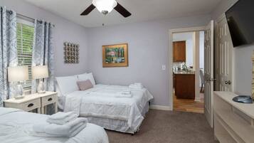 A bedroom with two beds, a ceiling fan, a painting, and a TV.