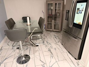 A modern kitchen with a glass dining table, chairs, a cabinet, and a refrigerator. - CHARMING ADULT RETREAT! (Pensacola)