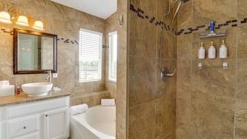 A bathroom with a bathtub, a shower, a vanity with a sink, and a mirror.