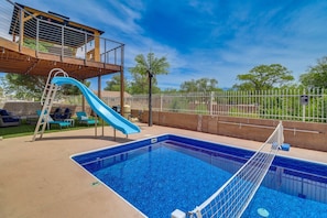 Una piscina con tobogán, un área de estar techada y un patio cercado.