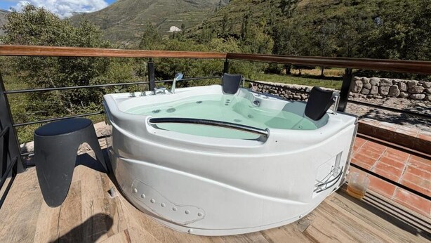 A hot tub on a wooden deck with a stone wall and a mountain view. - Auka Boutique (Urubamba)