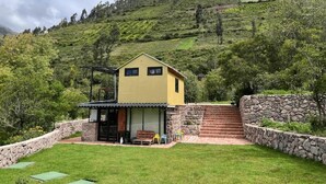 A yellow building with a patio area, stone steps, and a view of a green hillside. - Auka Boutique (Urubamba)