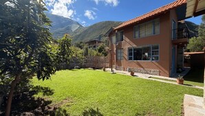 A two-story house with a well-maintained lawn, a stone wall, and a mountain backdrop. - Auka Boutique (Urubamba)