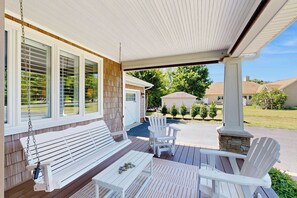Eine überdachte Veranda mit einer Bank, Adirondack-Stühlen und einem Tisch.
