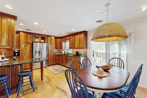 Eine moderne Küche mit Holzausbau, einem Edelstahlkühlschrank und einem Essbereich mit großem Tisch und blauen Stühlen.