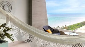 A hammock chair with a view of the ocean, a chair with a cushion, and a round table. - Luxury 2-bedroom Ocean view condo , Gym Spa & Infinity Pool (Cancún)