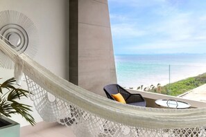 A hammock chair with a view of the ocean, a chair with a cushion, and a round table. - Luxury 2-bedroom Ocean view condo , Gym Spa & Infinity Pool (Cancún)