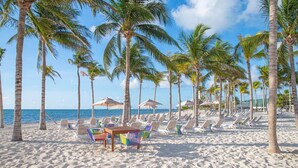 A beach with rows of palm trees, beach chairs, and umbrellas. - Luxury 2-bedroom Ocean view condo , Gym Spa & Infinity Pool (Cancún)
