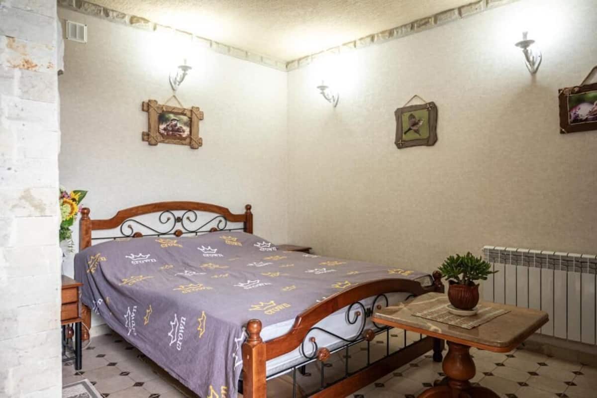 A bedroom with a wooden bed, a small table with a plant, and wall-mounted light fixtures.