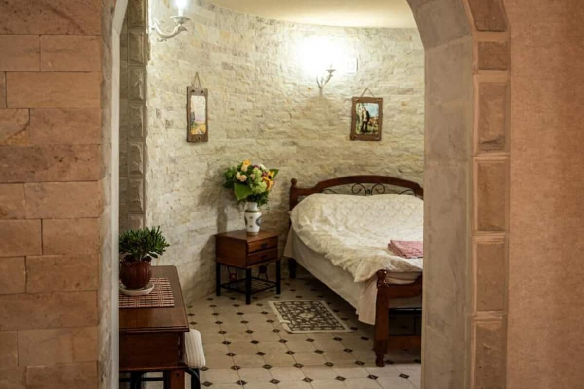 A bedroom with a bed, a nightstand, a potted plant, and a wall with pictures.