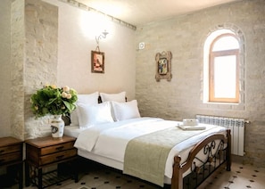 A bedroom with a bed, a nightstand, a vase with flowers, a window, and a radiator.