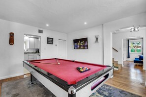 Ein Billardtisch mit roter Spielvliesbahn, ein Schussstöcke und ein Satz Billardkugeln.