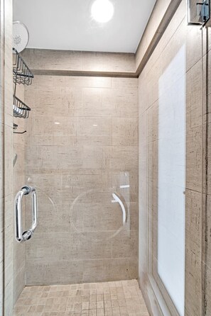 Eine Dusche mit beigen Fliesen, einer Glastür und einem Metallhandlauf.