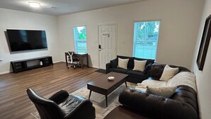 A living room with a flat-screen TV, a ceiling fan, a sofa, a coffee table, and a chair. - Phenomenal 3-bedroom townhome with AC in Houston (Houston)