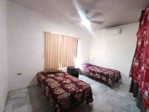 A room with two beds, a ceiling fan, a window with curtains, and an air conditioning unit. - Casa Paisa Planta Alta (Linares)