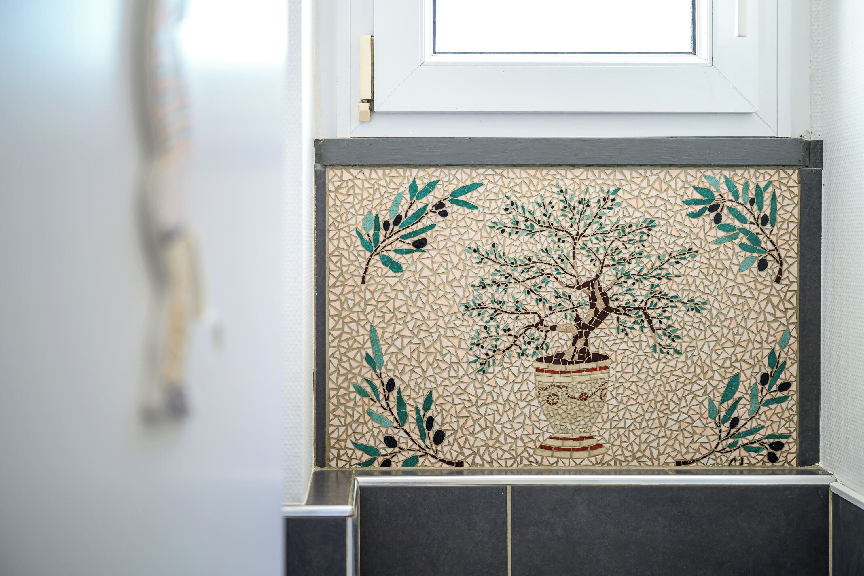 A tiled wall with a mosaic of a tree and leaves.