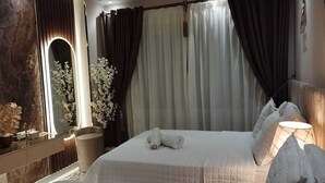 Et soveværelse med en stor seng, et natbord, et spejl og et vindue med gardiner.