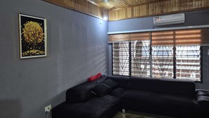 A room with a wooden ceiling, a black sectional sofa, a framed picture on the wall, and a window with blinds. - Lux, Spacious, apt, close 2 the beach and Airport. (Greater Accra Region)