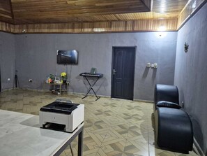 Ein Zimmer mit Fliesenboden, einem Drucker, einer Tastatur, einem Fernseher und einer Tür.