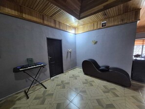 Ein Zimmer mit einem Klavier, einem schwarzen Stuhl, einer Tür und einem gemusterten Boden.