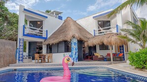 Une maison moderne avec une piscine, un toit de chaume et un flotteur en forme de flamant rose.