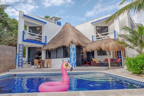 A modern house with a swimming pool, a thatched roof, and a pink flamingo float. - Dazzling Beachfront Villa, Pool, 3 king bedrooms (Q.R.)
