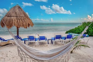 A beach with a hammock, blue lounge chairs, and a thatched umbrella. - Dazzling Beachfront Villa, Pool, 3 king bedrooms (Q.R.)