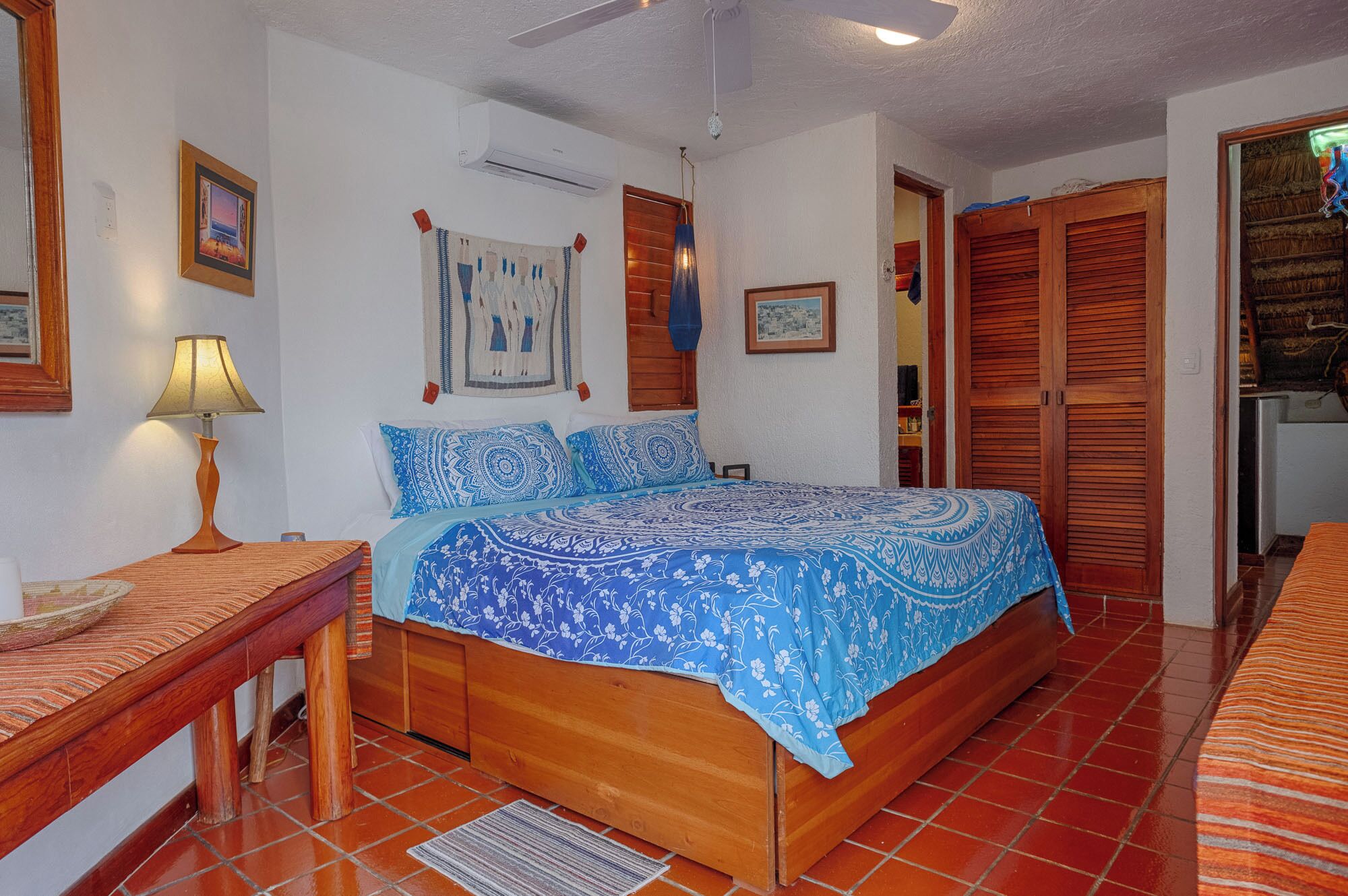 Une chambre à coucher comprenant un lit, une table de chevet, une lampe, un climatiseur mural et une armoire.