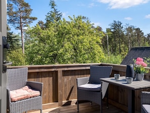 An outdoor deck with wicker furniture and a table, surrounded by a wooden fence and trees.