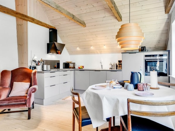 A modern kitchen with white cabinets, a dining table set for four, and a wooden ceiling.