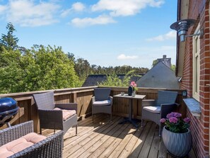 Eine Holzterrasse mit Korbmöbeln, einem Grill und einem Topfpflanzen.