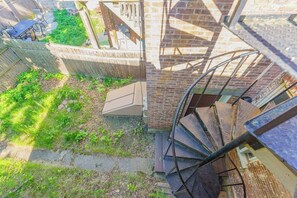 Una escalera en espiral conduce a una terraza con un muro de ladrillo y un espacio cerrado con una mesa y sillas.