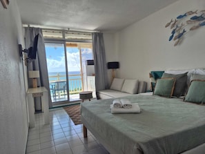 Habitación de hotel con cama, sofá, televisión, balcón con vistas al océano y una obra de arte en el techo.