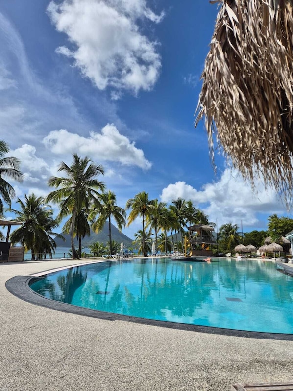 Una piscina azul cristalina rodeada de palmeras y una montaña al fondo.