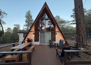 A triangular wooden structure with string lights, a sliding glass door, and a grill outside. - Quaint 2-bedroom A-Frame Cabin in Sugarloaf/Big Bear for a relaxing getaway. (Big Bear)