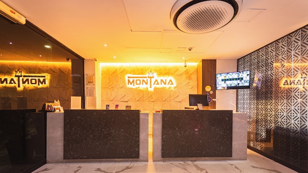 A reception area with a marble floor, two reception desks, a wall-mounted TV, and a patterned wall design. - Hotel Montana (Bello)