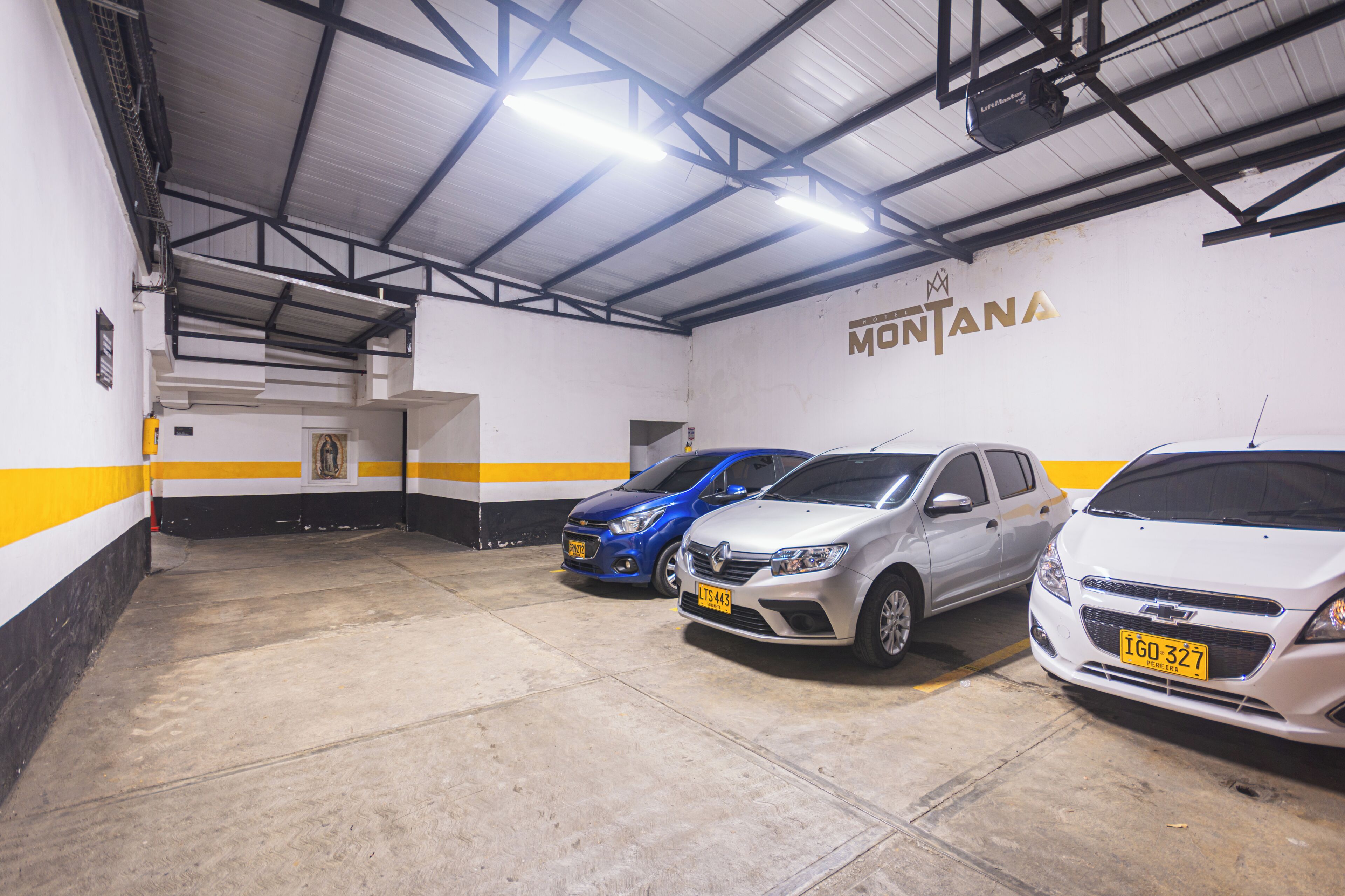A parking garage with three cars, a metal roof, and a wall with the text 'MONTANA'.