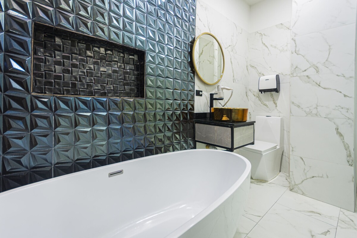 Un baño moderno con una bañera independiente, un espejo, un secador de manos y un inodoro.
